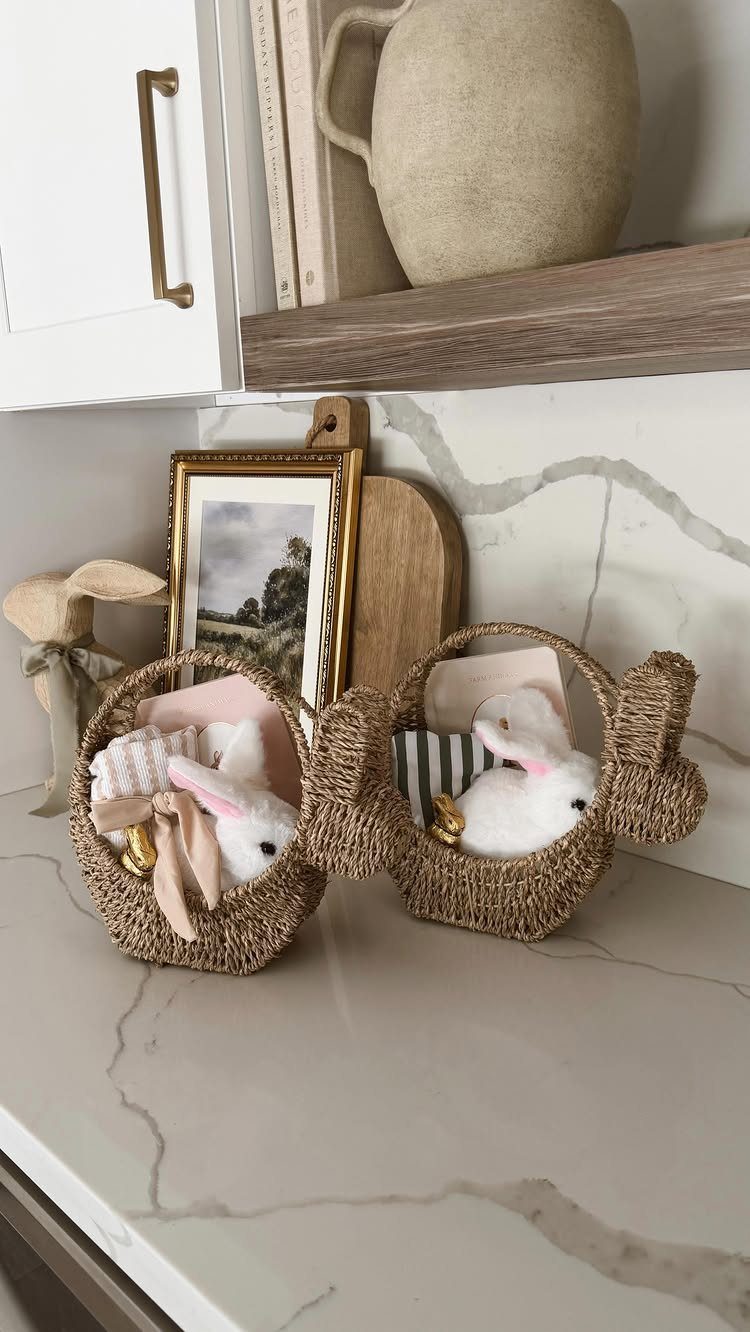 Two woven bunny-shaped baskets with plush white rabbits on a marble counter.