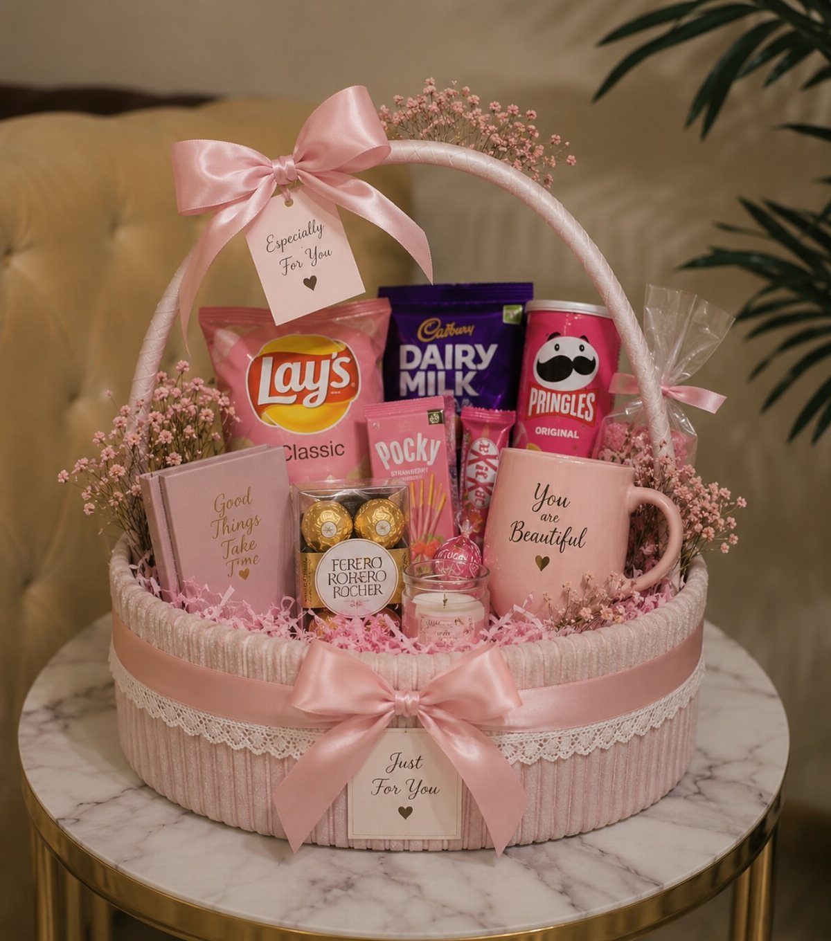 Pink gift basket filled with assorted chocolates, chips, and a decorative mug.