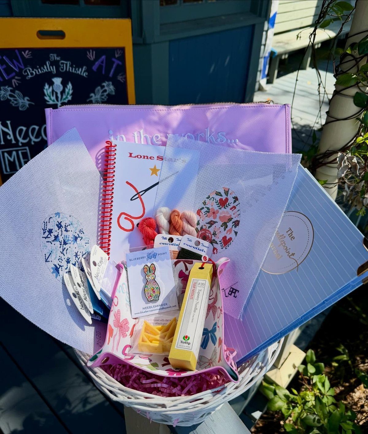 White wicker gift basket containing a blue journal, notebook, and bunny-shaped soap.