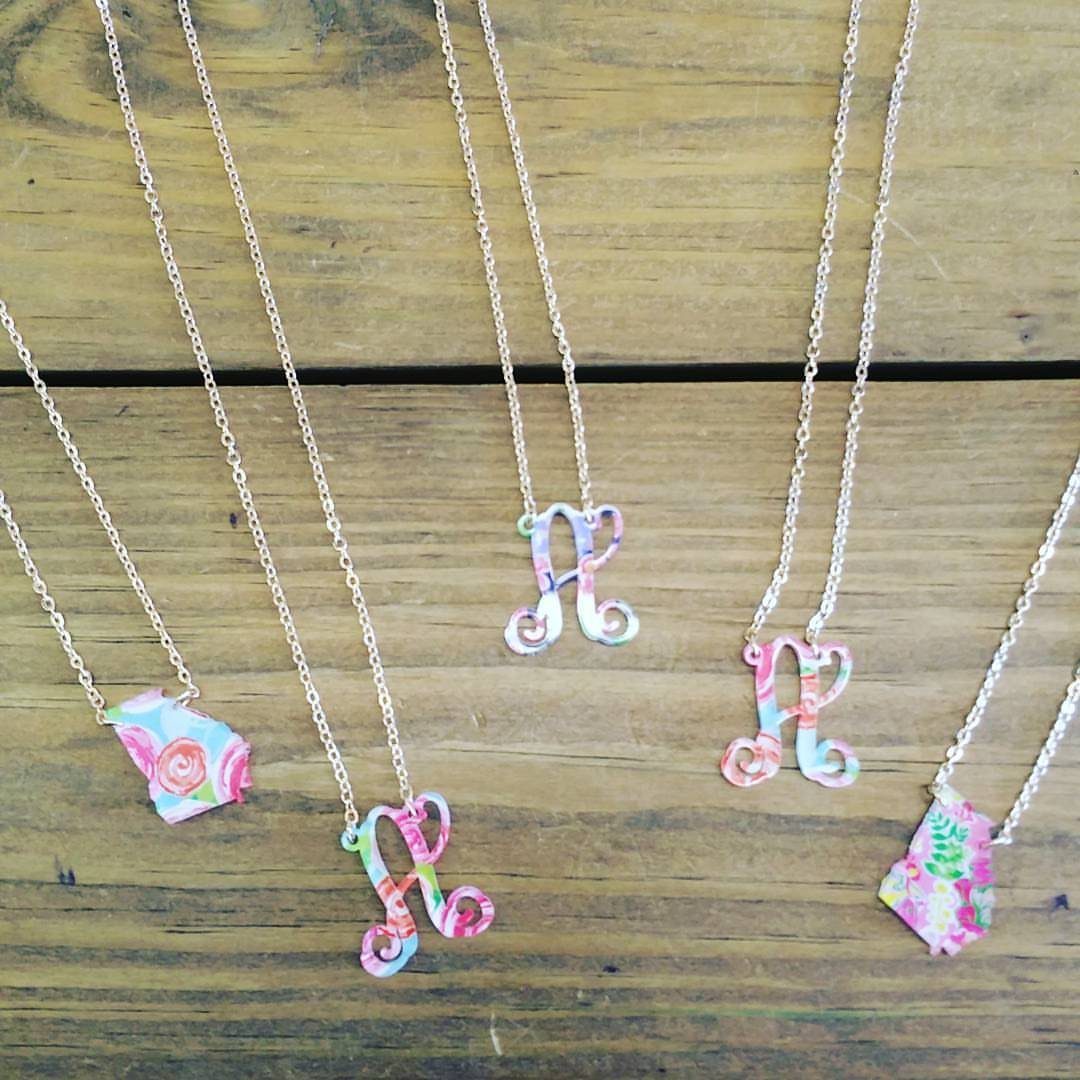 Silver necklaces with colorful floral initial pendants resting on a wooden background