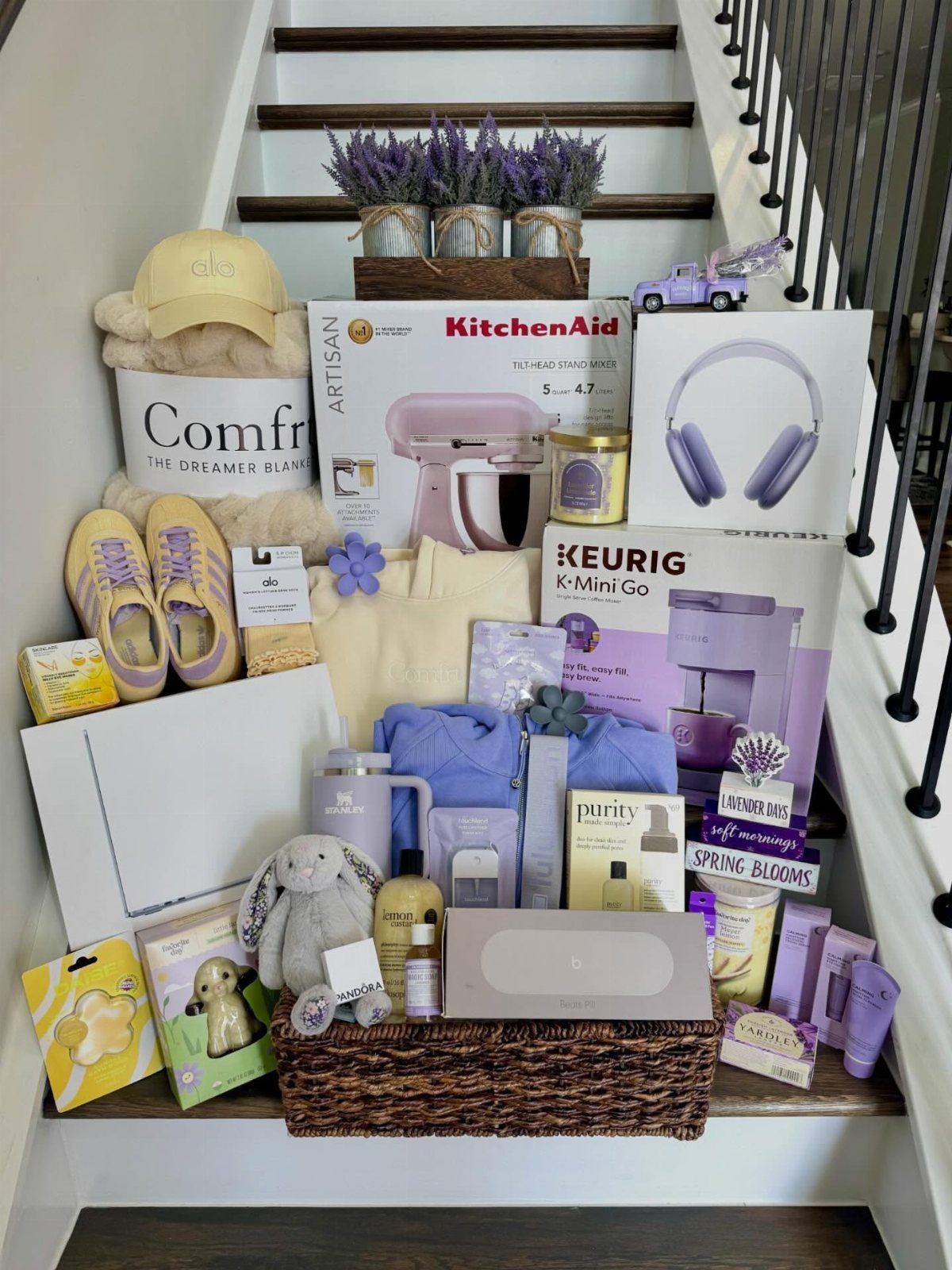 Assorted luxury gifts and beauty products arranged on stairs with a wicker basket.