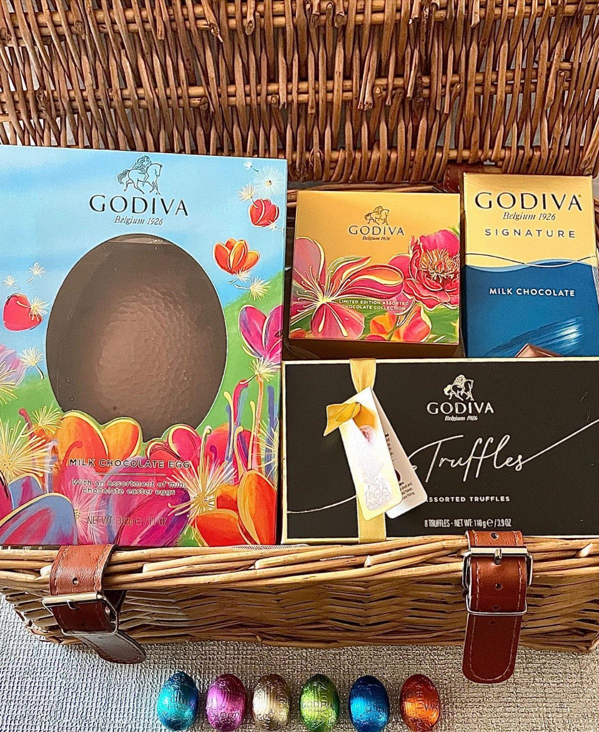 Godiva chocolate boxes and colorful foil eggs inside a woven wicker Easter basket