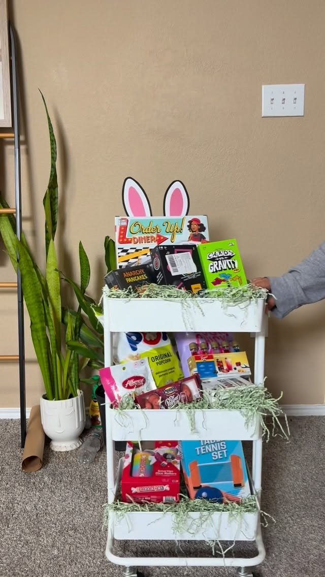 White rolling cart filled with board games and snacks for an Easter basket.