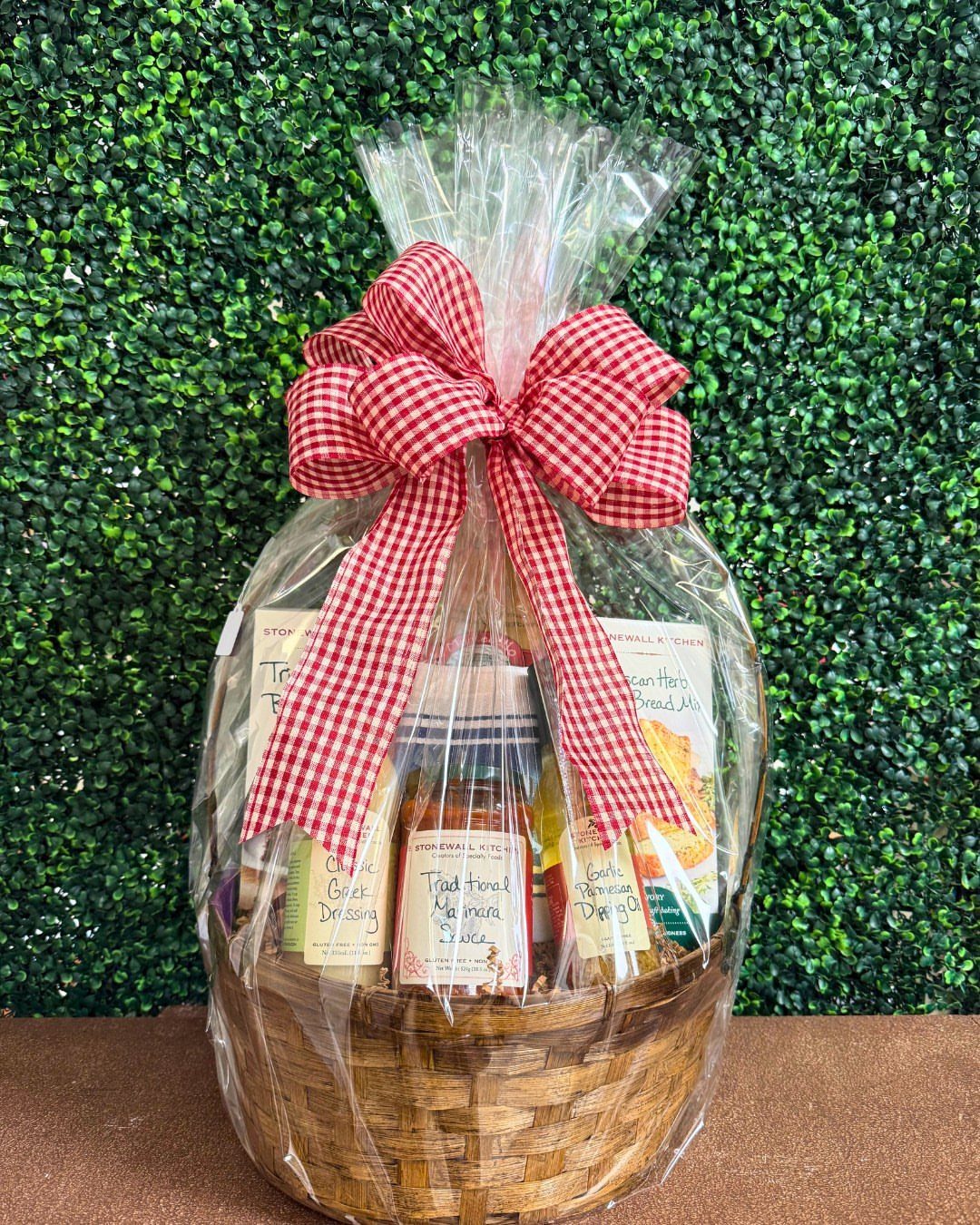 Woven wicker gift basket with gourmet foods wrapped in cellophane and red bow.