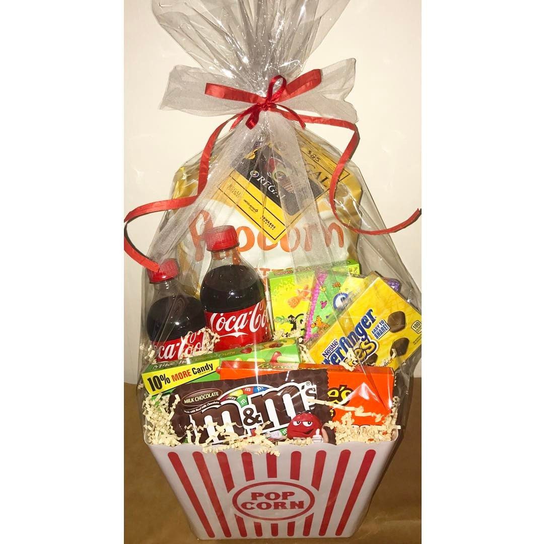Popcorn bucket gift basket filled with candies and soda wrapped in clear cellophane.