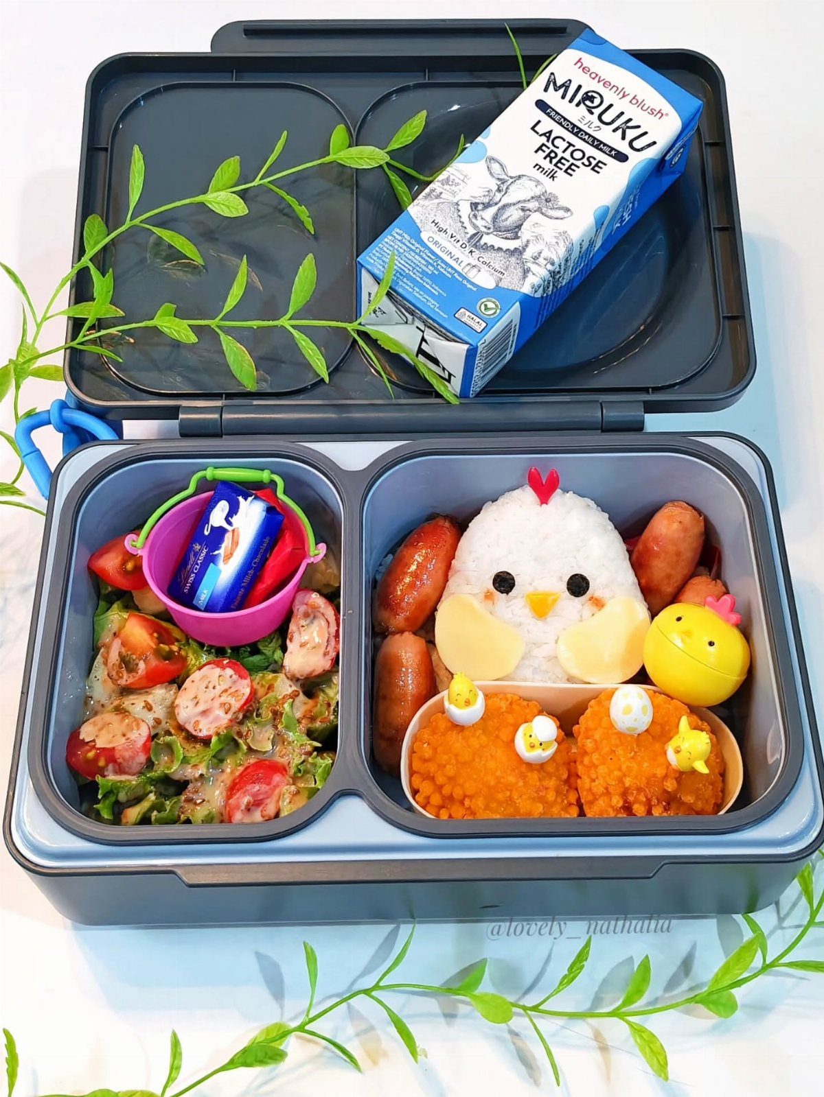 Bento-style lunch box with chick-shaped rice, salad, and a carton of milk.