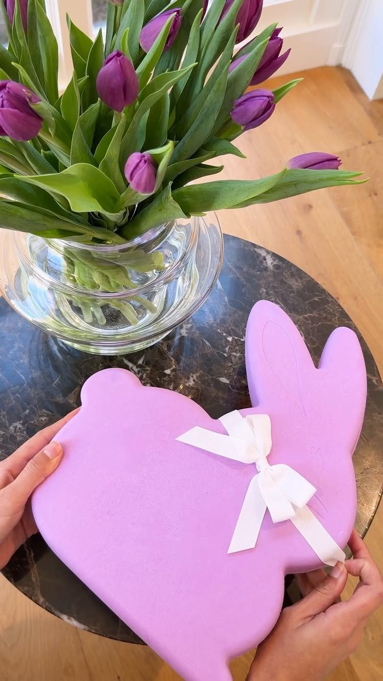 Purple bunny-shaped gift box with white ribbon next to purple tulips in vase