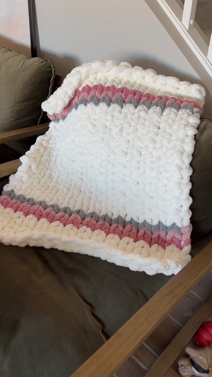 Chunky knit white blanket with pink and grey stripes on a brown sofa