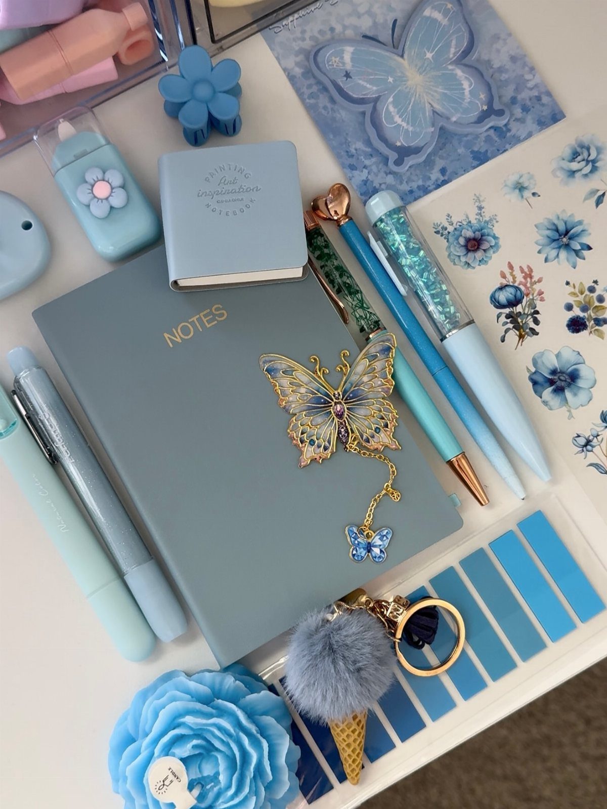 Blue notebook and matching pens with butterfly accessories and stationery on white surface