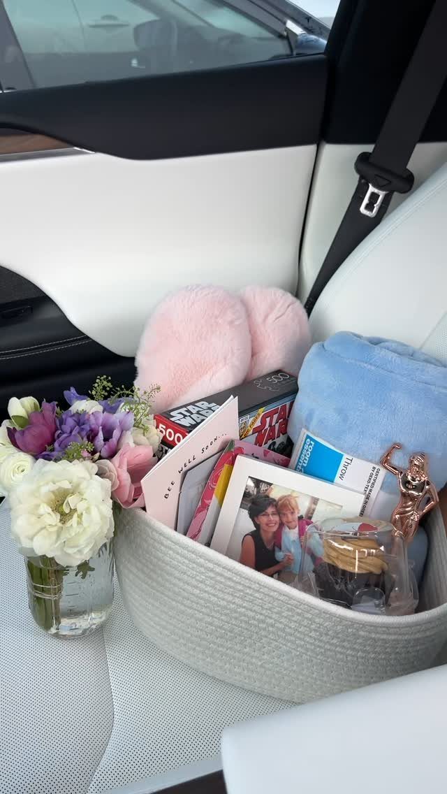 White woven gift basket with pink slippers and flowers inside a car