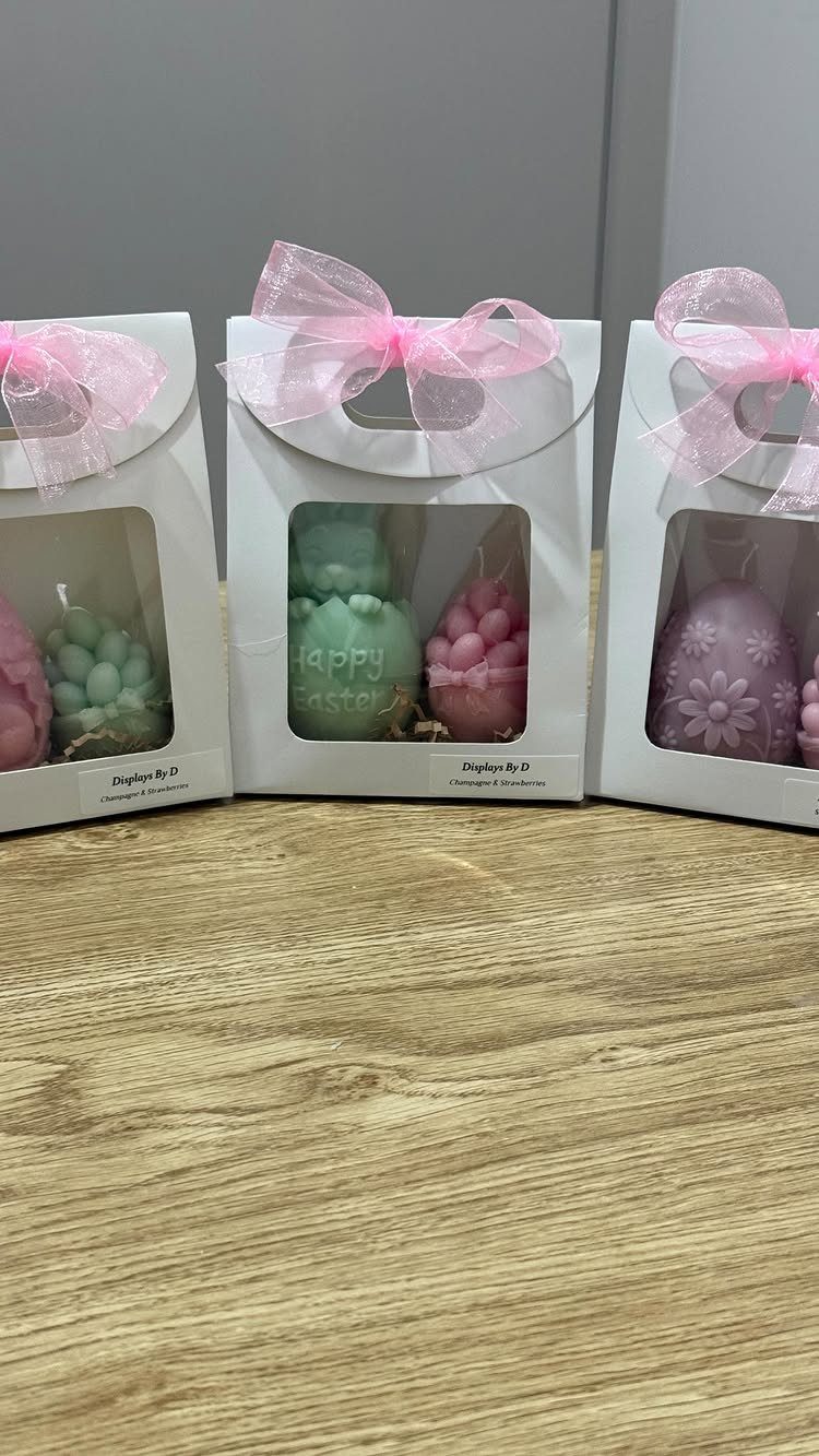 Colorful bubble candles in white gift boxes with pink bows on wooden surface