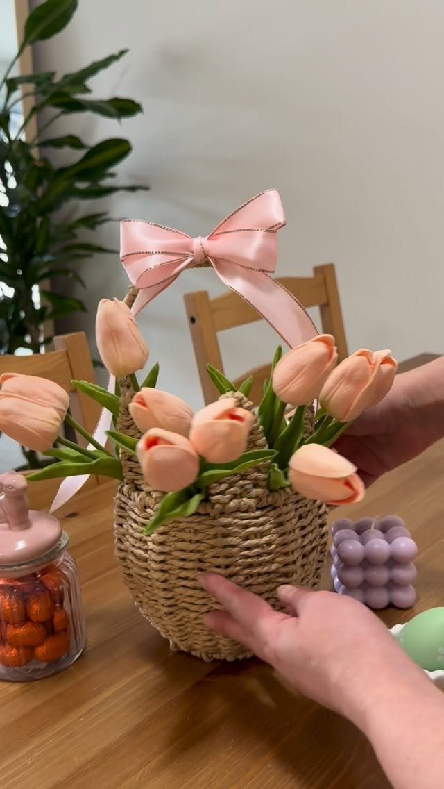 Woven wicker basket filled with peach tulips and a pink bow on a table