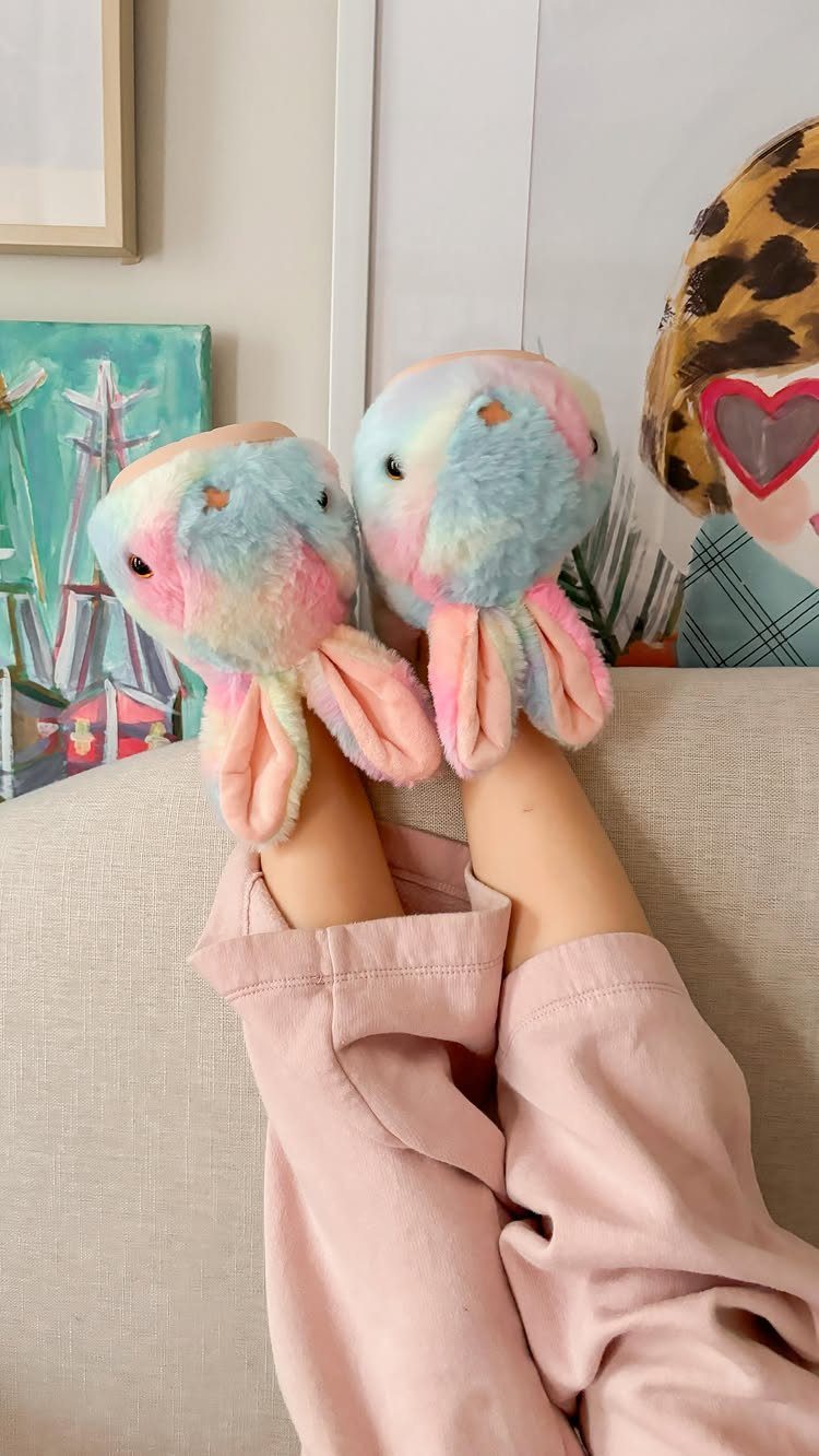 Pastel blue and pink fluffy bunny slippers worn by a person resting legs.