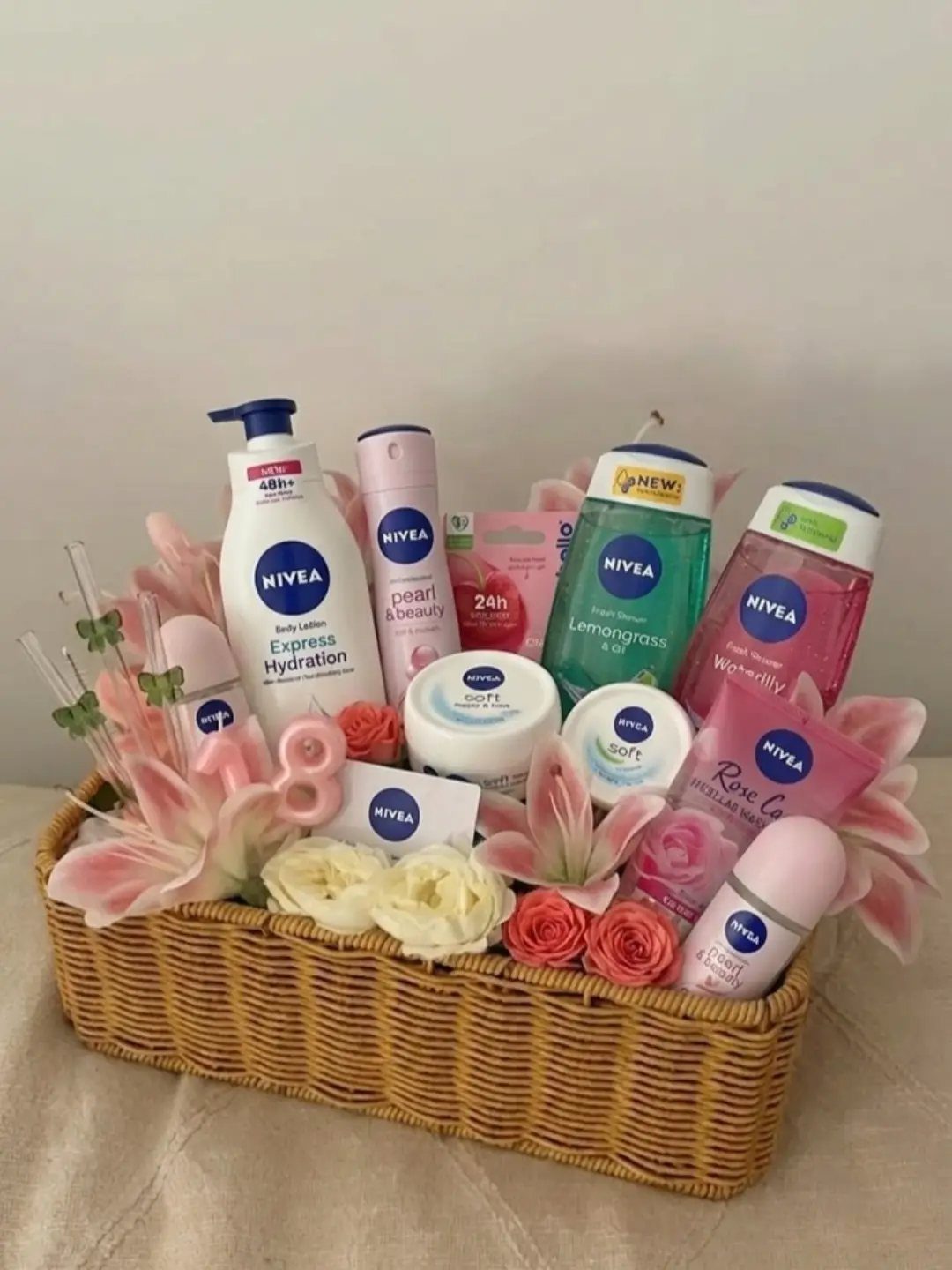 Woven basket filled with Nivea skincare products and pink and white artificial flowers.