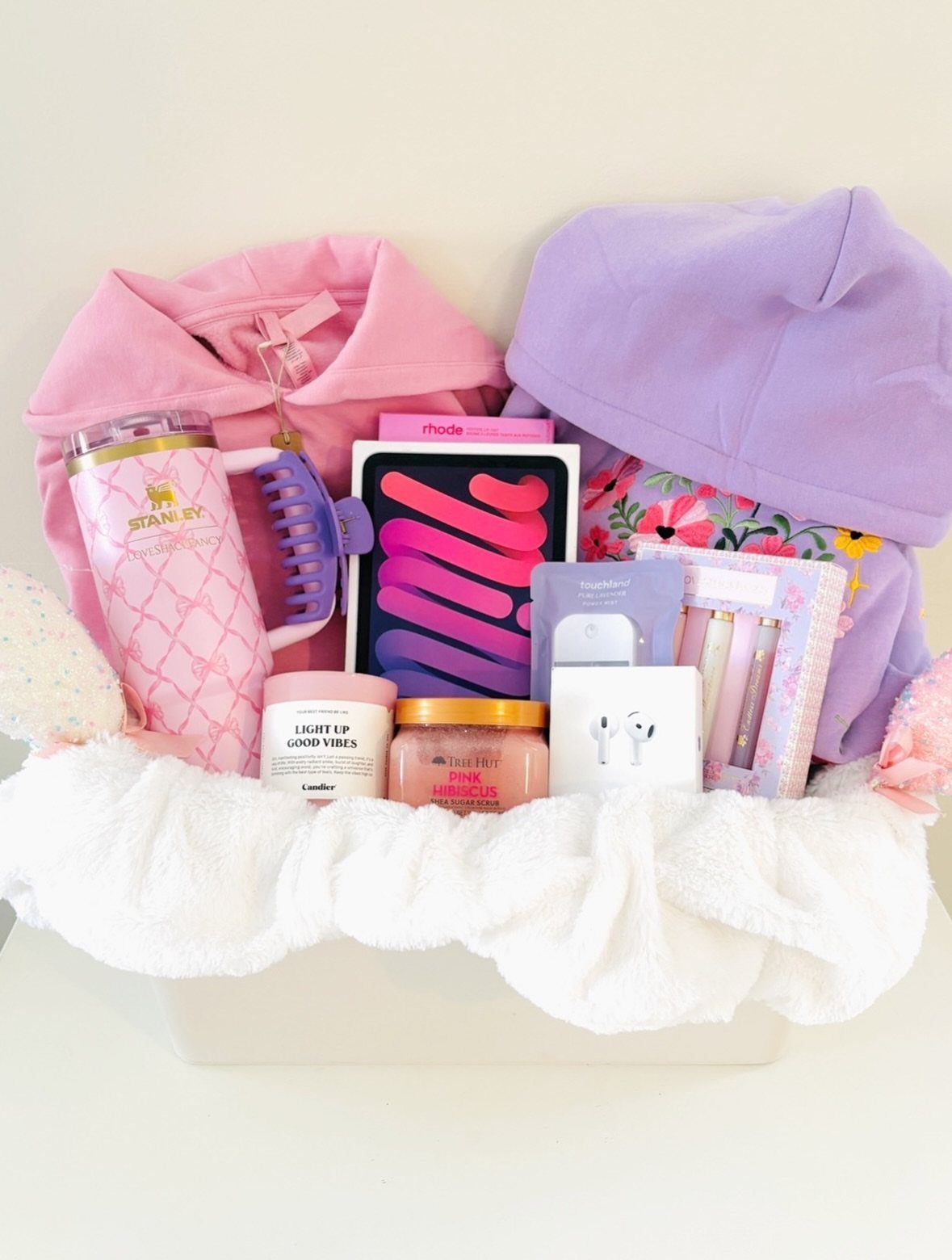 Pink and purple gift basket with tumbler, clothing, and skincare on white background.