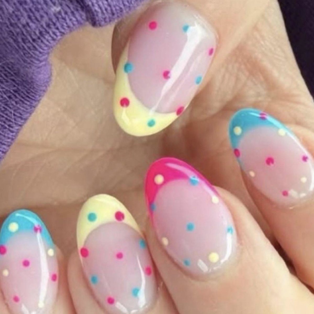Almond shaped nails with nude base, multicolored polka dots and pastel French tips.