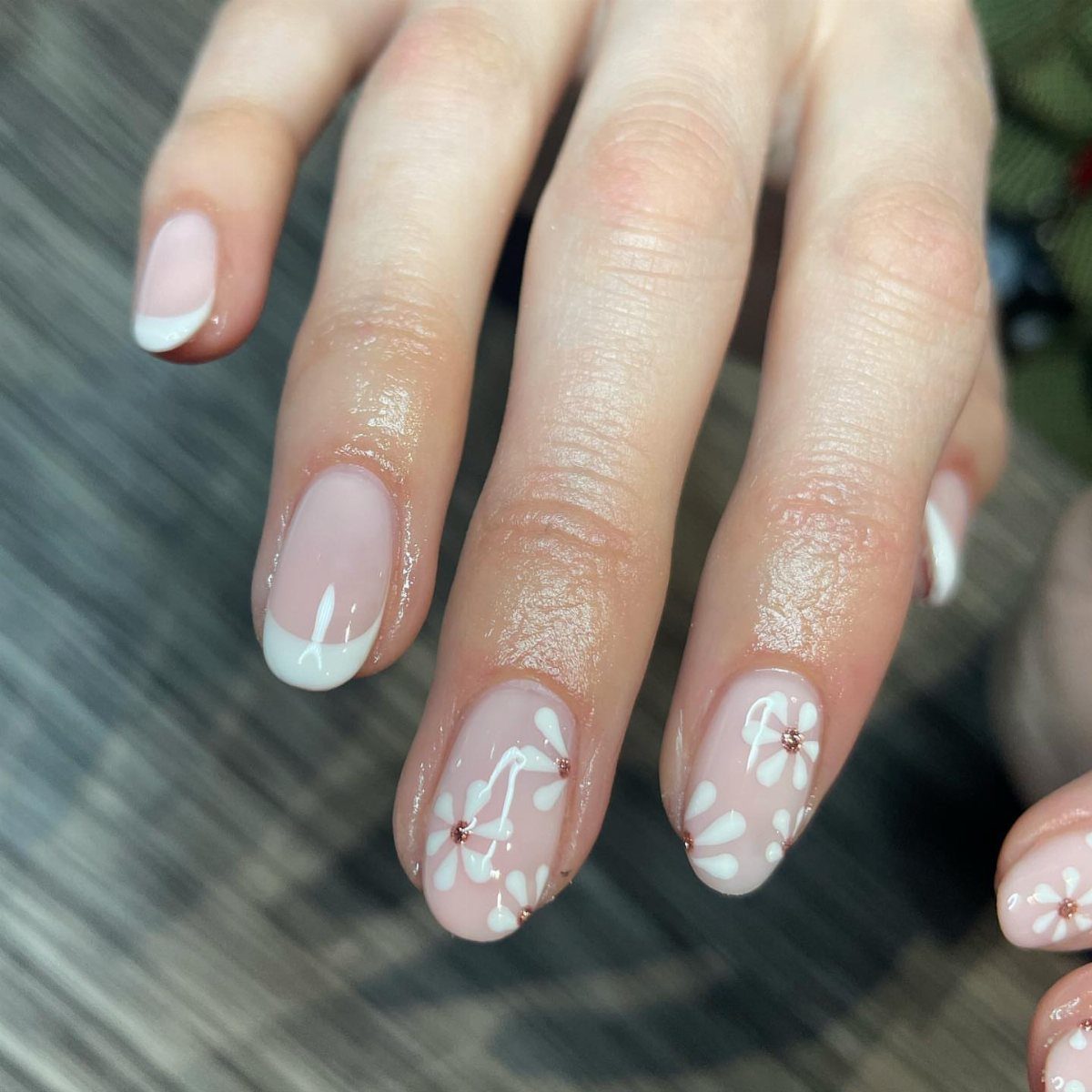 Almond shaped nails with nude base, white French tips, and white daisy floral accents.