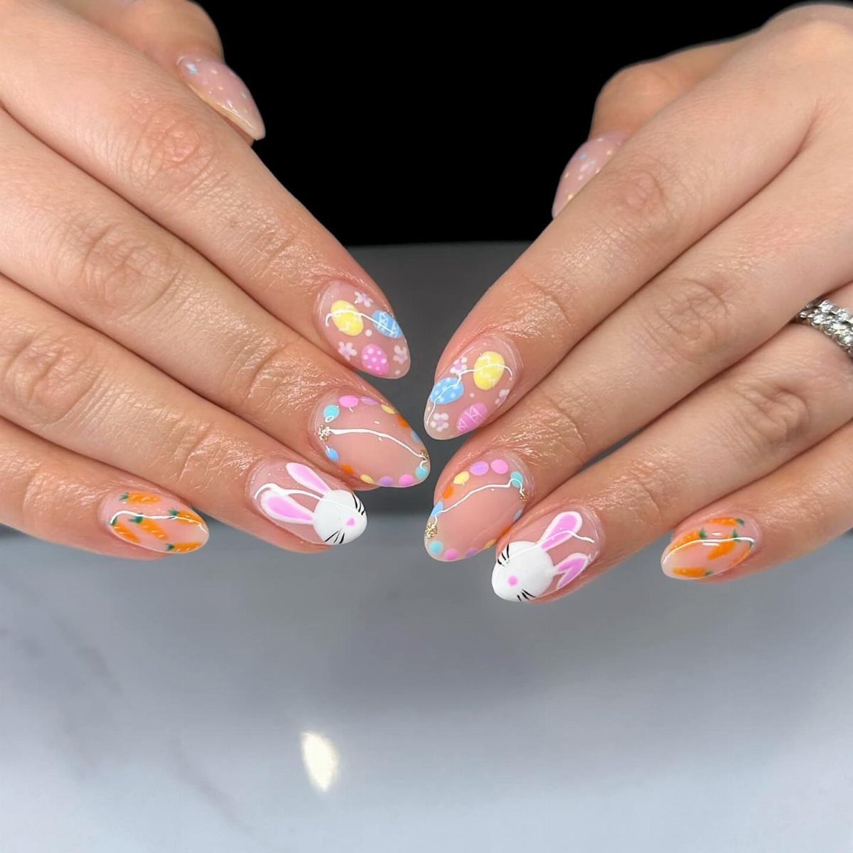 Almond shaped nails with nude base featuring pastel eggs and bunny nail art.