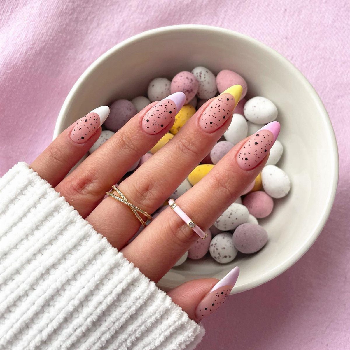 Almond shaped nails with pastel speckled polish resting on a bowl of candy eggs.