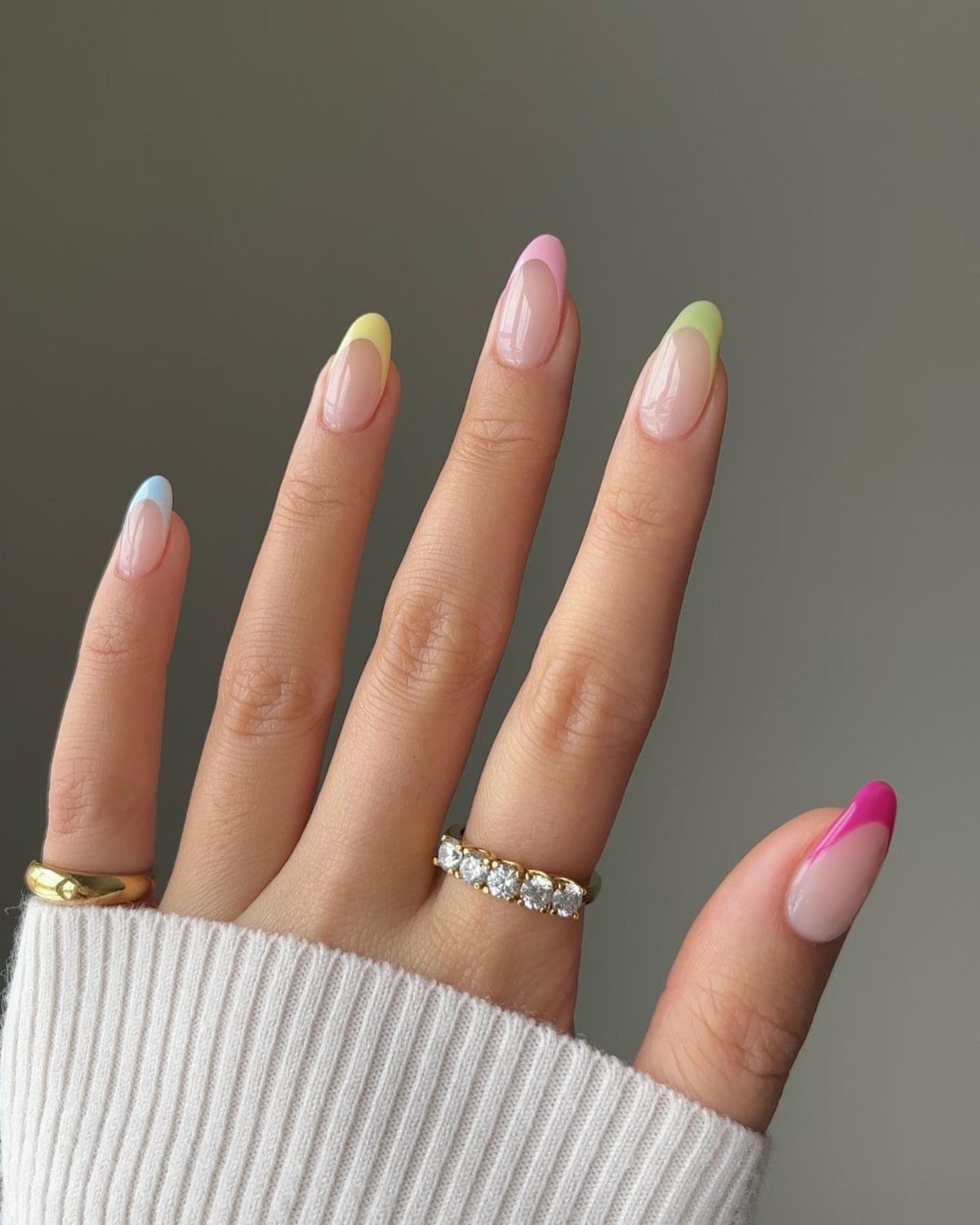Almond-shaped nails with nude base and multi-colored pastel French tips on a hand.
