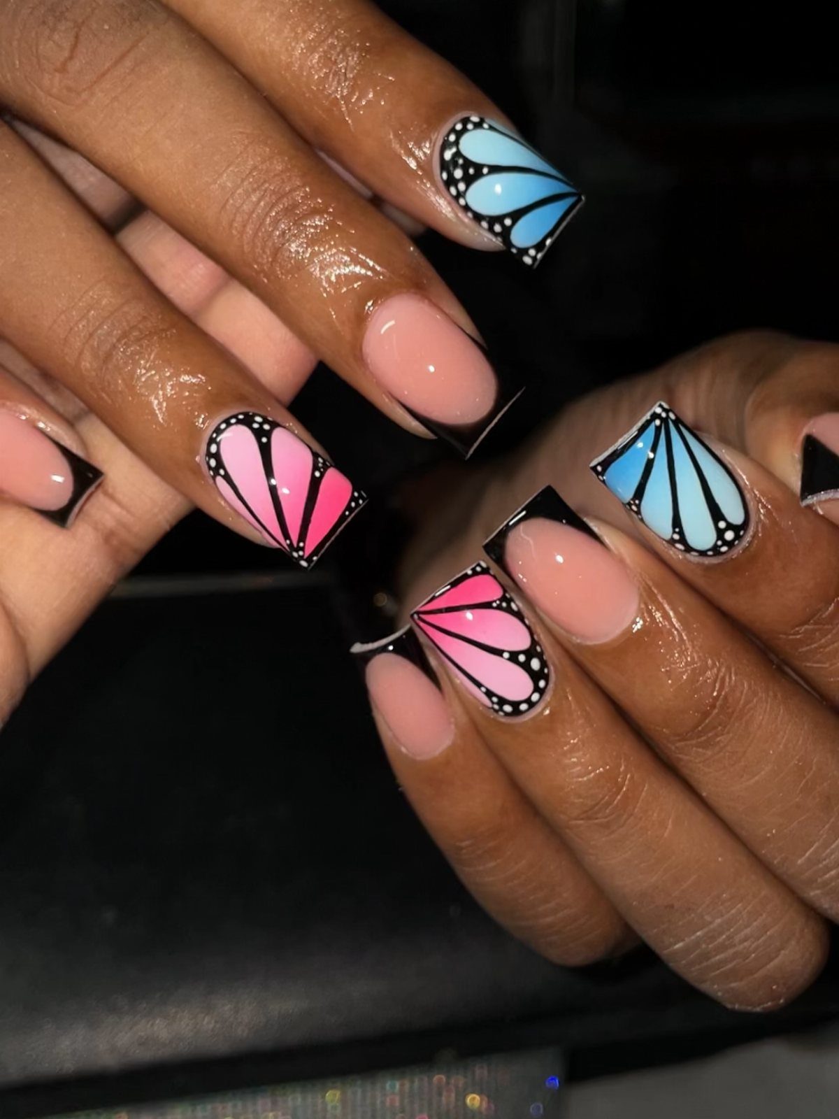 Nails with blue and pink butterfly wing art and nude polish.