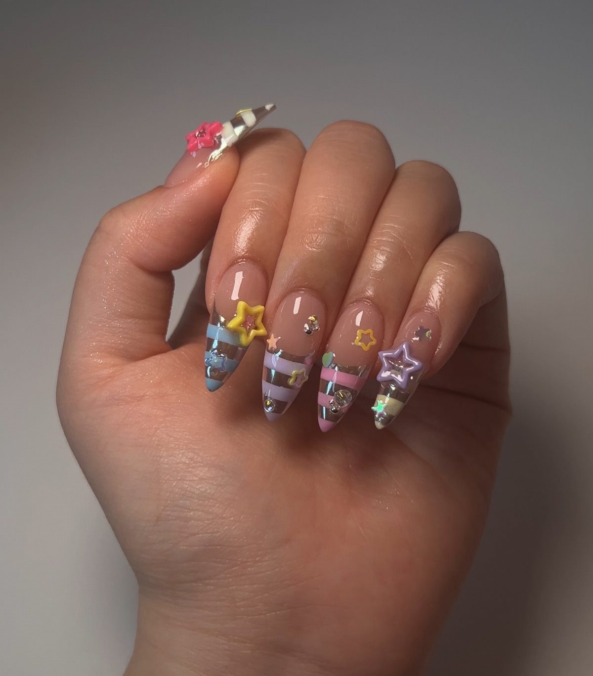 Pastel striped nails with 3D star charms and glitter on almond-shaped tips.