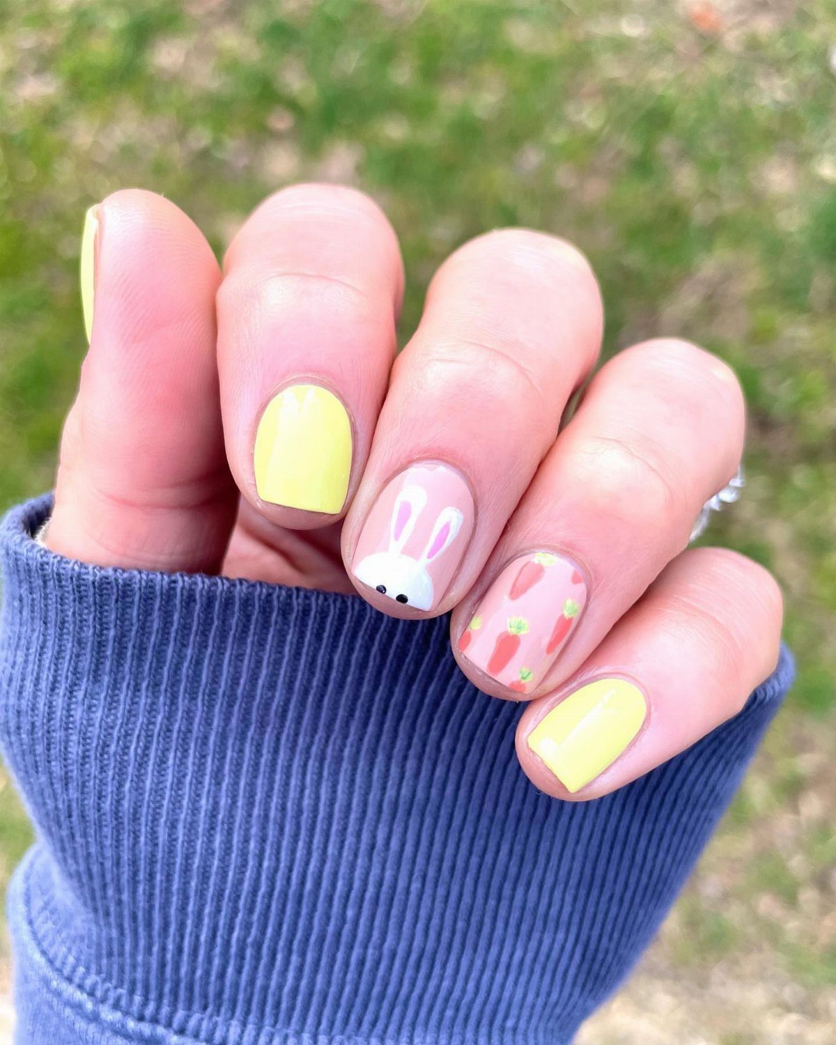 Manicured nails with pastel yellow polish, a bunny face, and tiny orange carrots.
