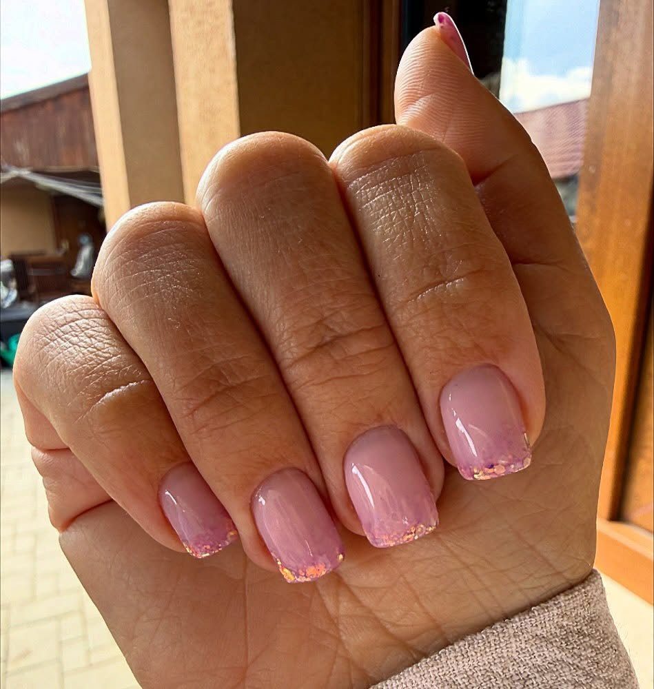 Light pink nails with a shimmering gold and pink glitter ombre effect.