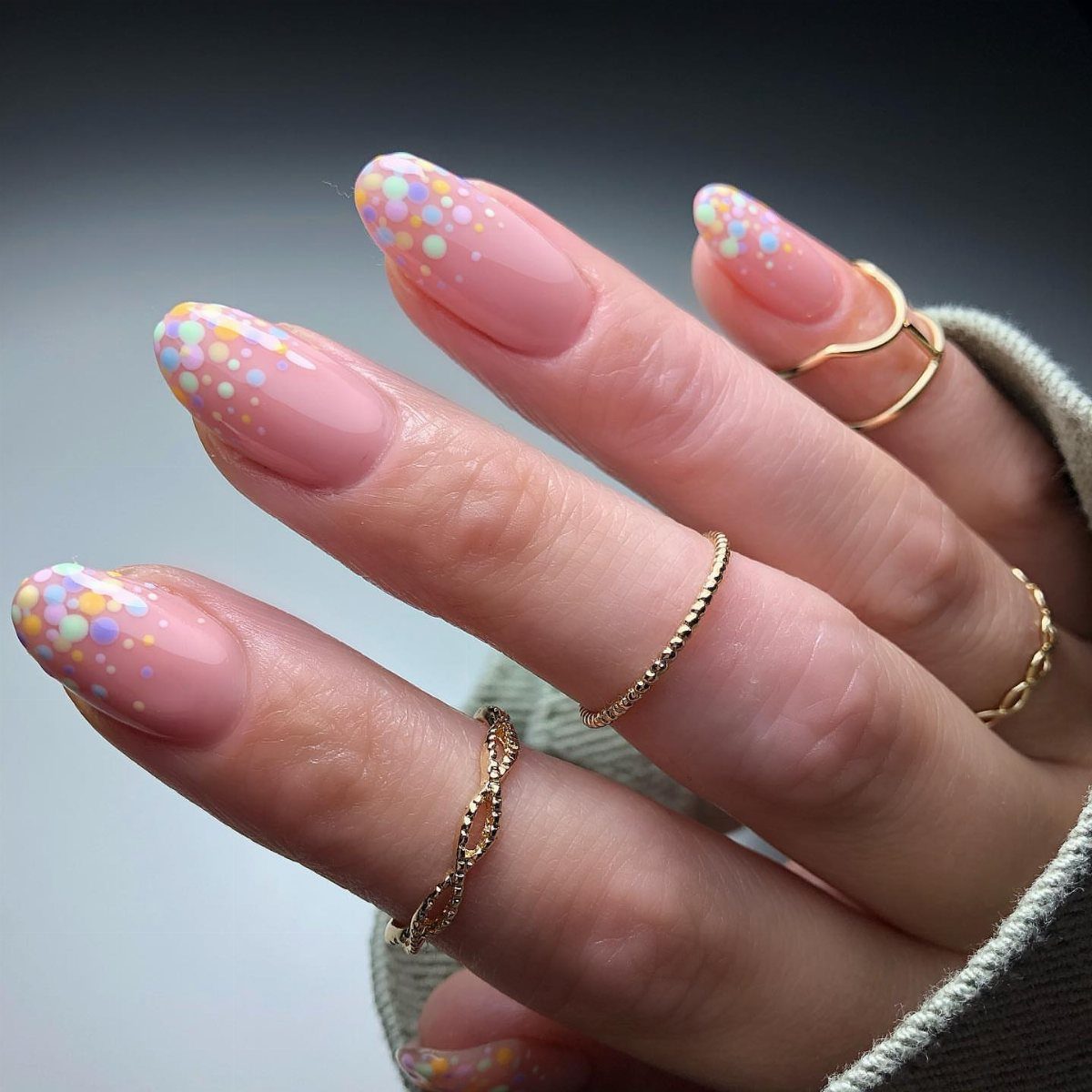 Almond-shaped nails with nude base and multicolored pastel polka dots at the tips.