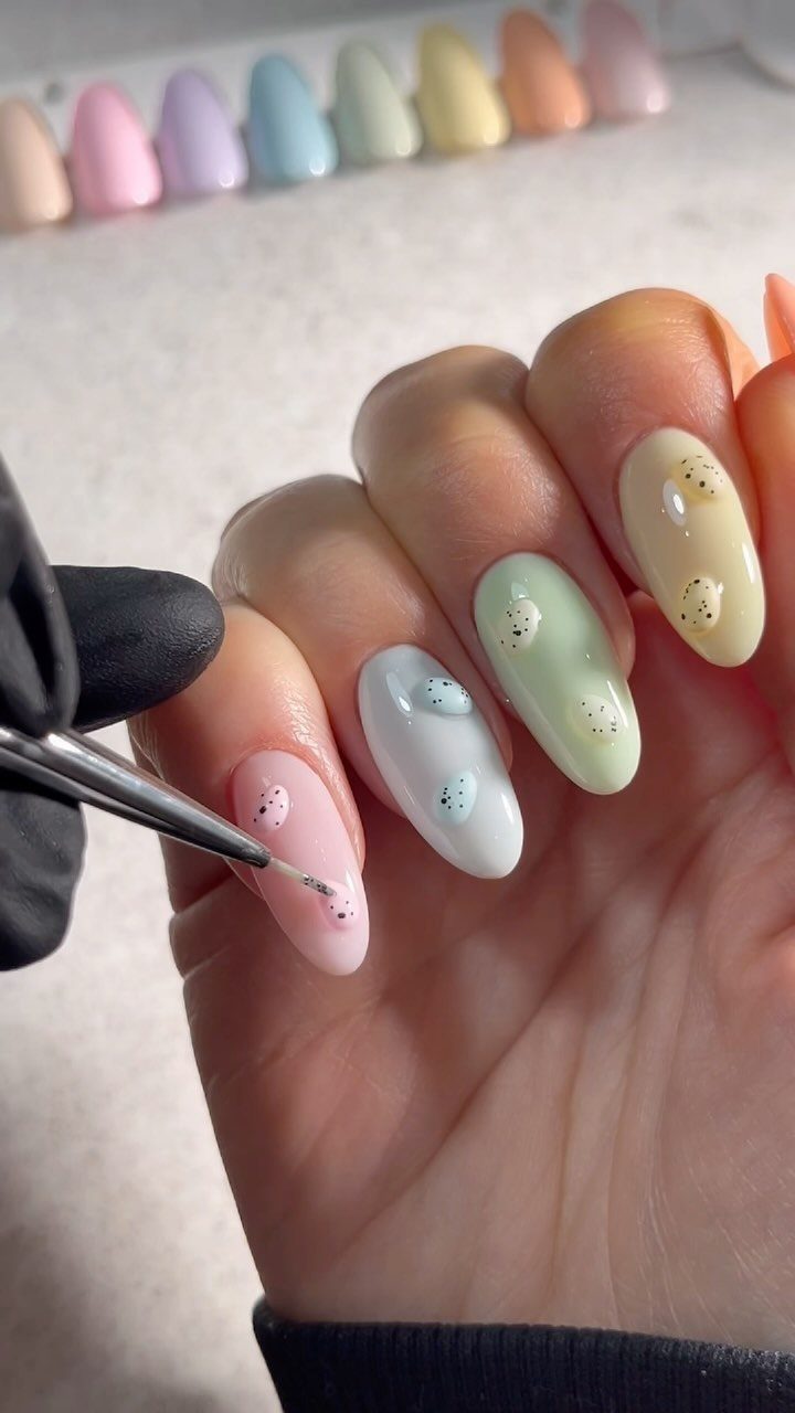 Pastel colored almond nails with dark speckles resembling Easter eggs being painted.
