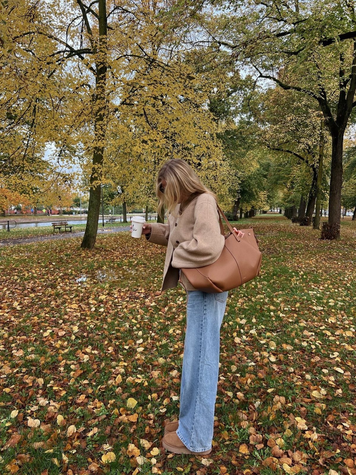 Woman in beige cardigan, wide-leg jeans, and tan boots standing in autumn park.