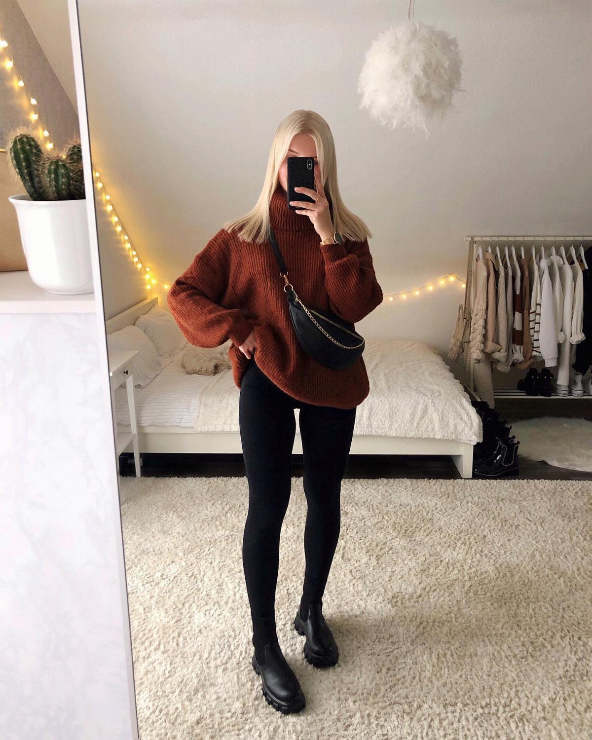 Woman wearing an oversized rust sweater and black leggings in a bedroom mirror selfie