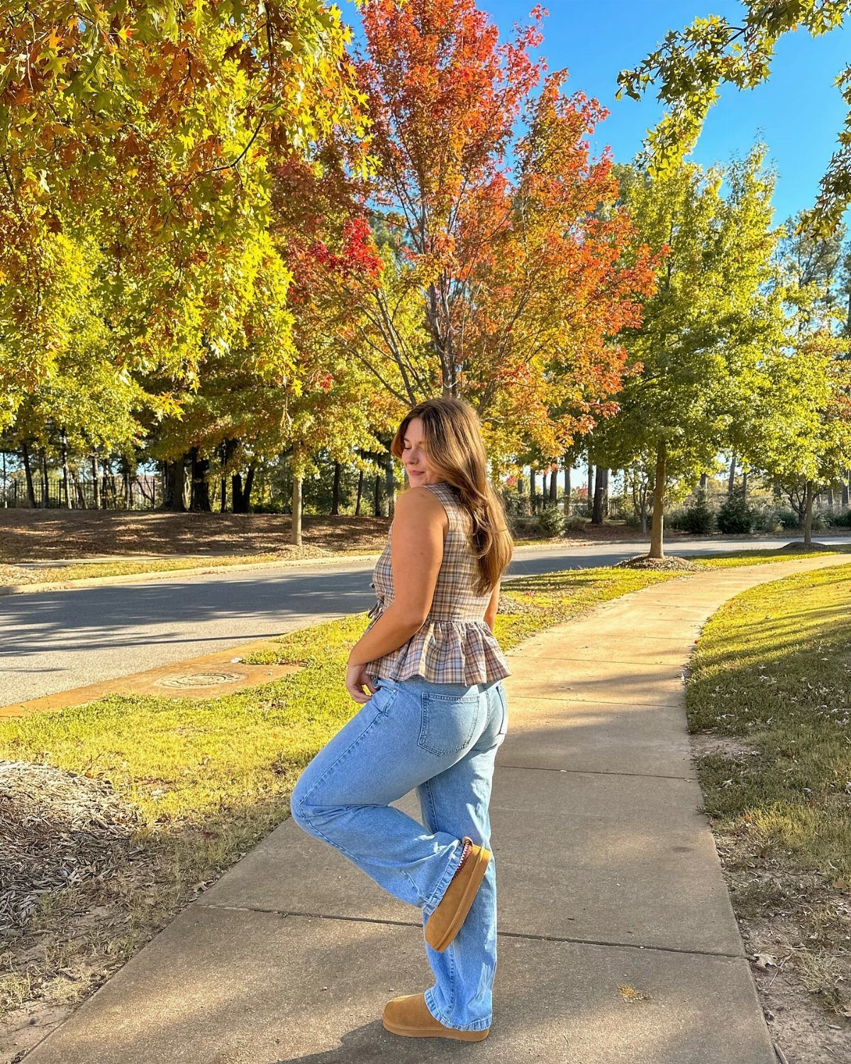 Woman in plaid peplum top and wide-leg jeans standing on autumn sidewalk
