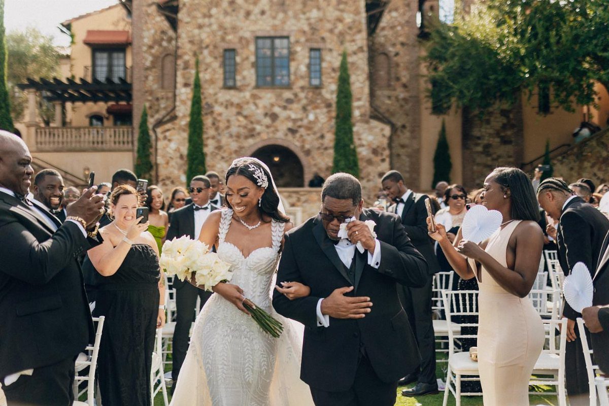 Bride in white gown and father in black tuxedo walking down wedding aisle