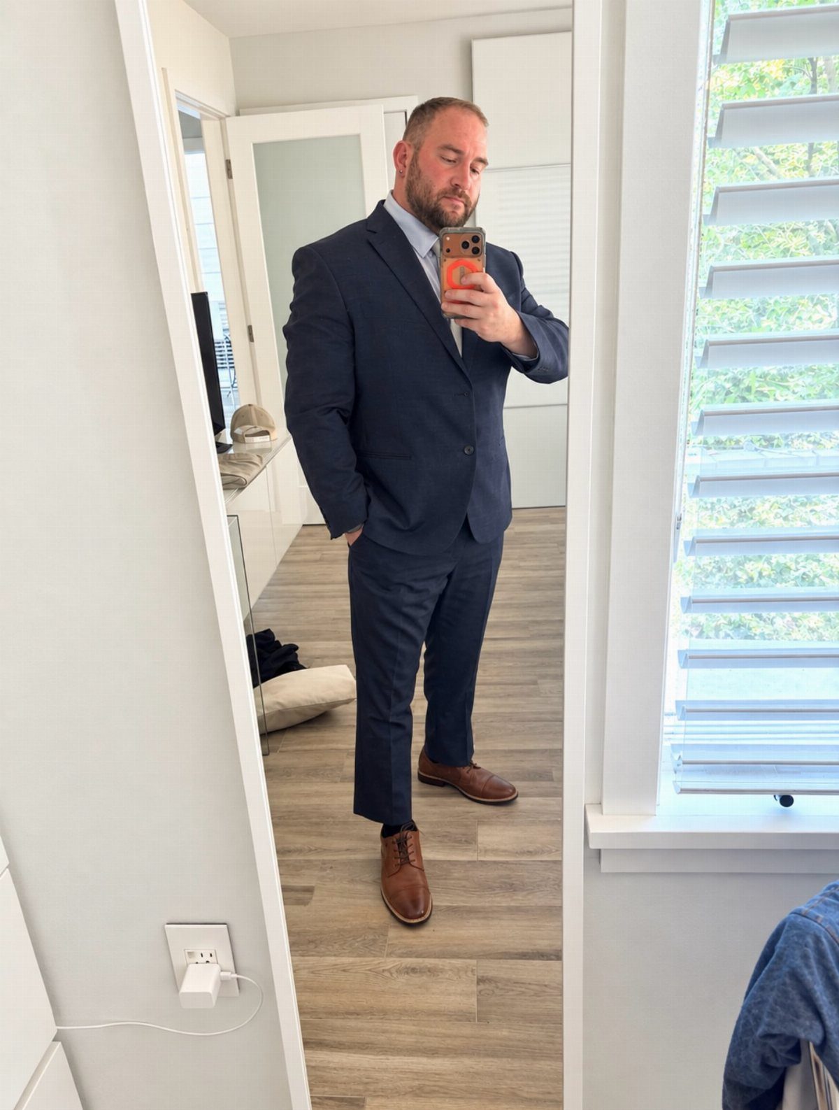 Man in a navy blue suit and brown shoes taking a mirror selfie.