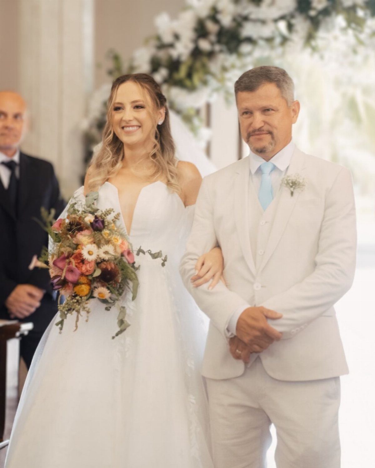 Bride in white gown walking with father wearing a white wedding suit