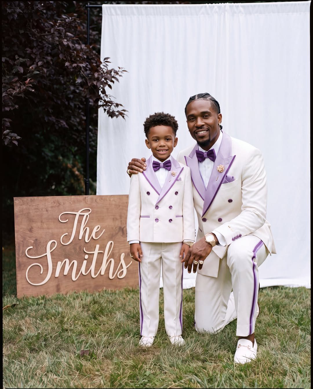 Man and boy in matching white suits with purple accents posing outdoors.