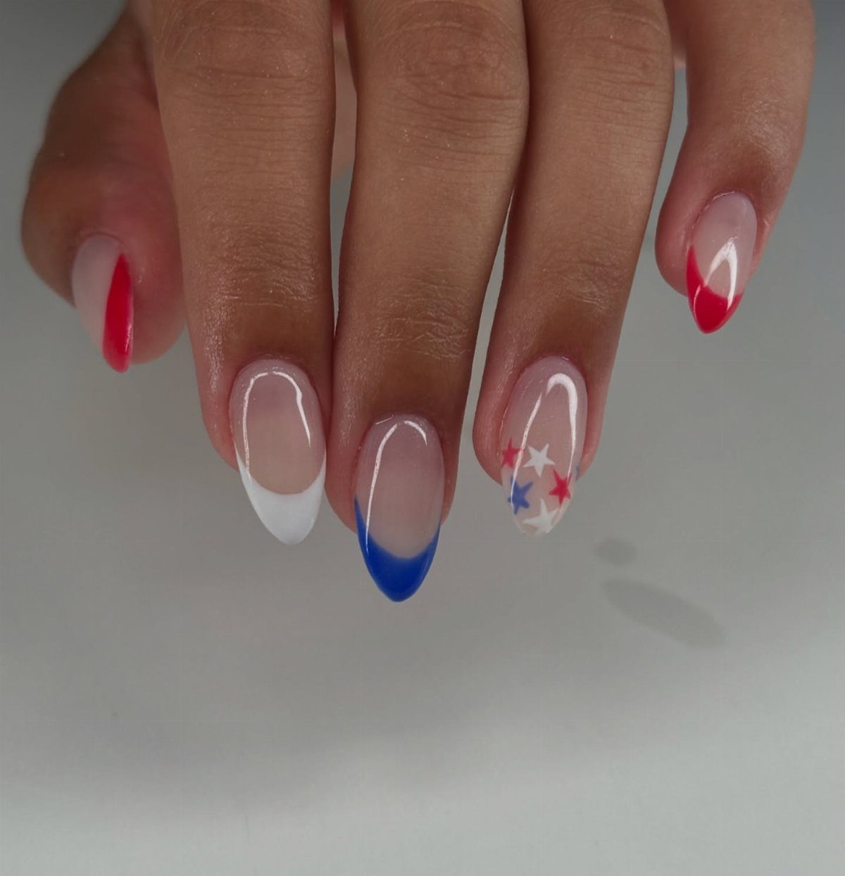 Nude almond nails with alternating red, white, and blue French tips and stars.
