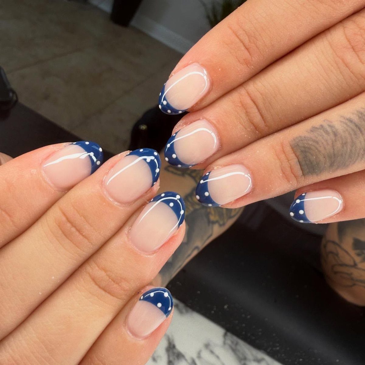 Manicured nails with blue French tips and small white polka dots on nude base.