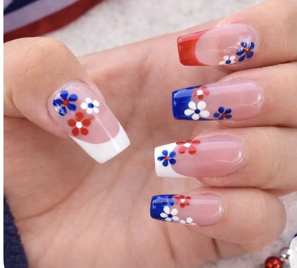 Nails with red, white, and blue French tips and small floral designs.