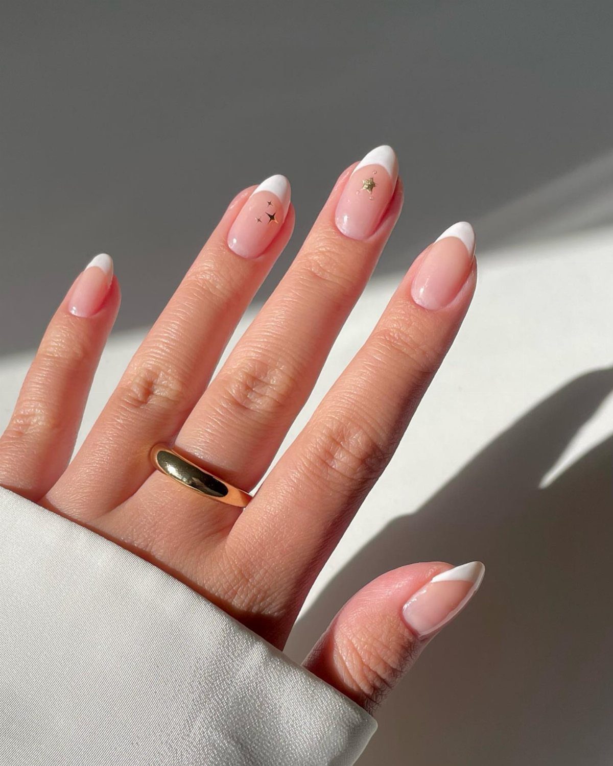 Nude French tip nails with small gold star accents and a gold ring.