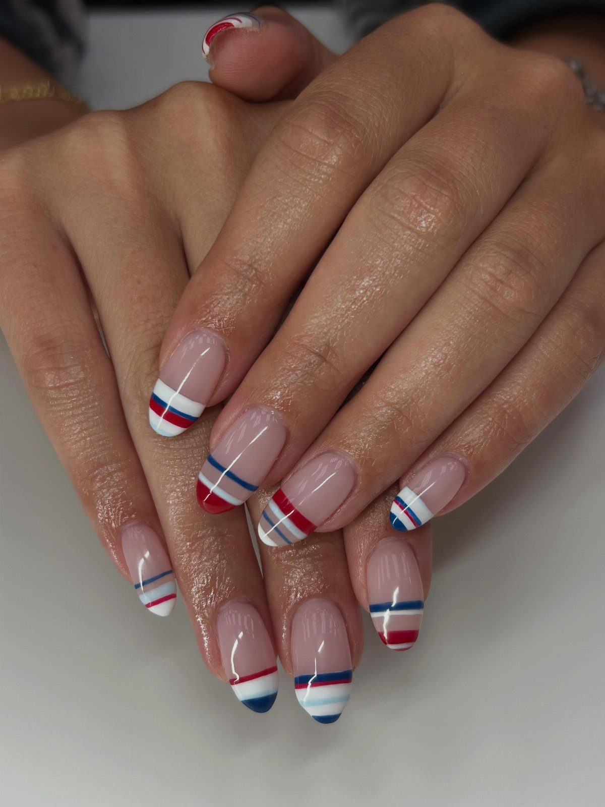 Nude nails with red, white, and blue striped French tips on hands.