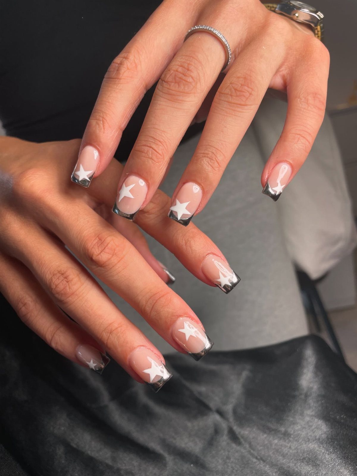 Almond nails with nude base, silver chrome French tips and white star designs.