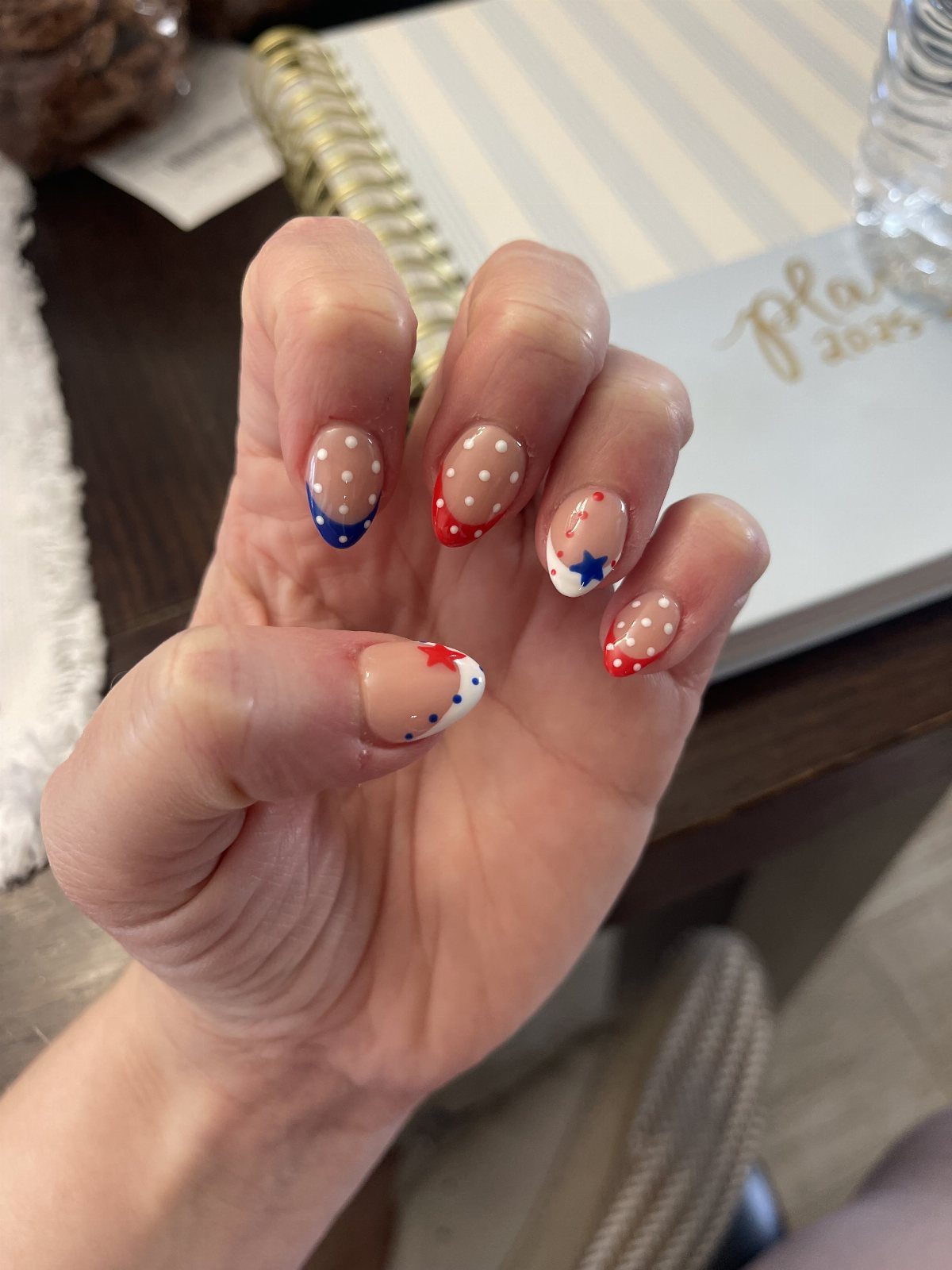 Nude nails with red and blue French tips, white polka dots, and stars.