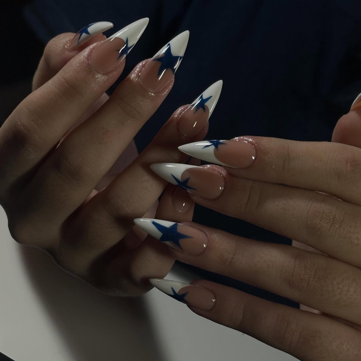 Almond-shaped nails with white French tips and blue stars on nude base