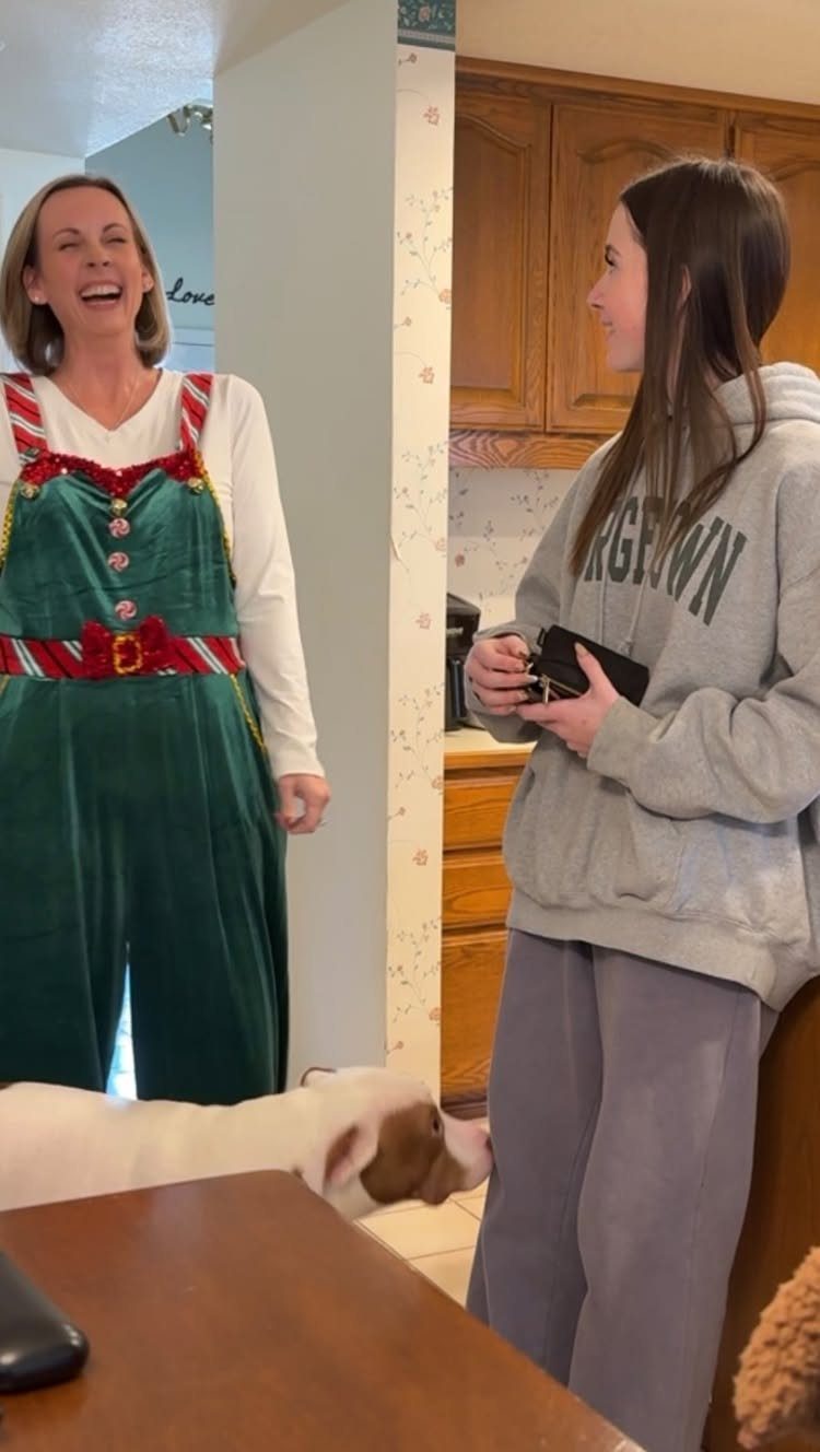Woman in a green velvet elf costume laughing with a teenage girl in a kitchen