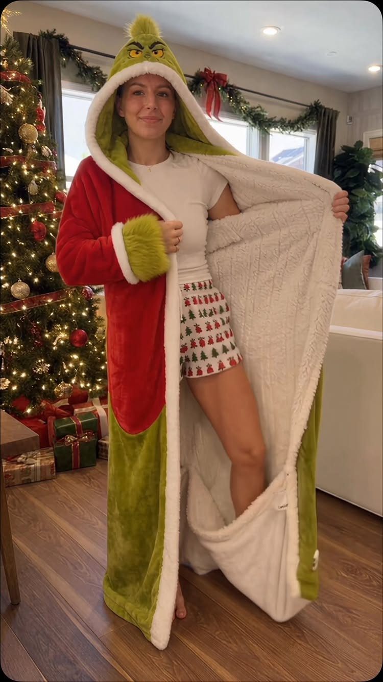 Woman wearing a Grinch hooded robe and Christmas shorts by a decorated tree