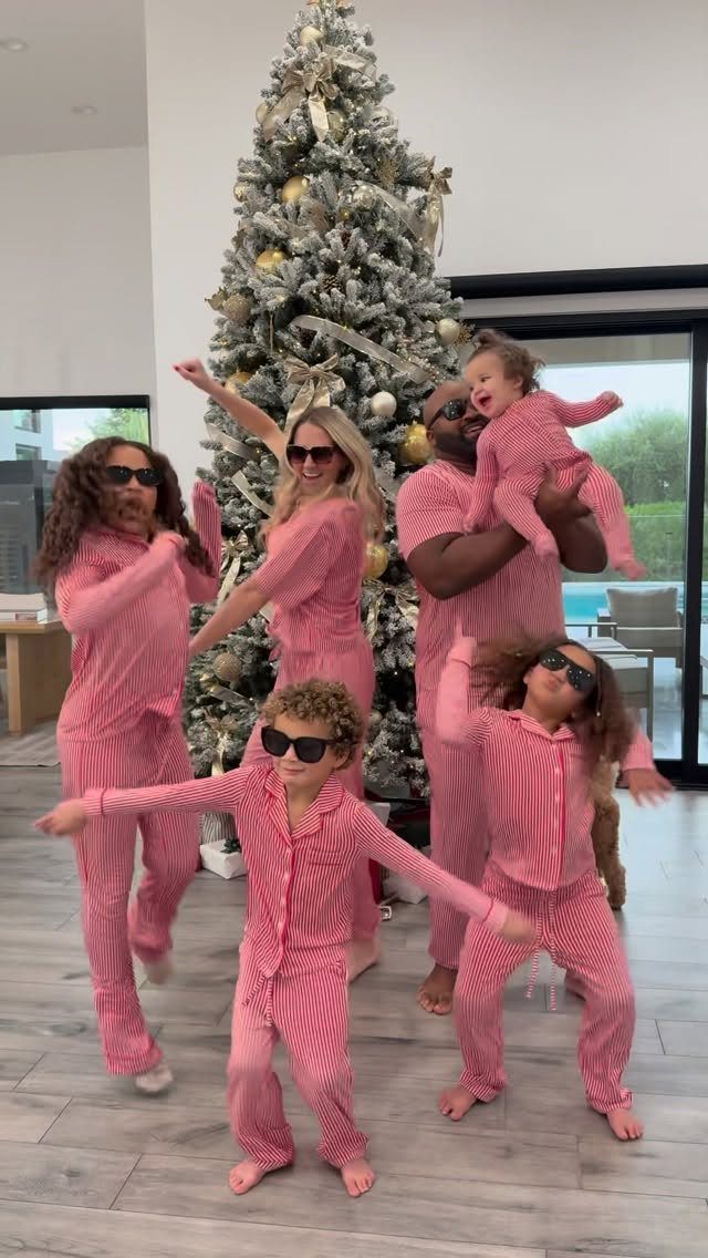 Family wearing matching red and white striped pajamas posing by a Christmas tree