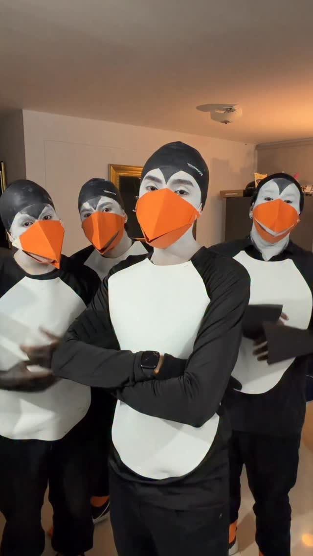 Four people wearing matching penguin costumes with orange beak masks posing indoors.