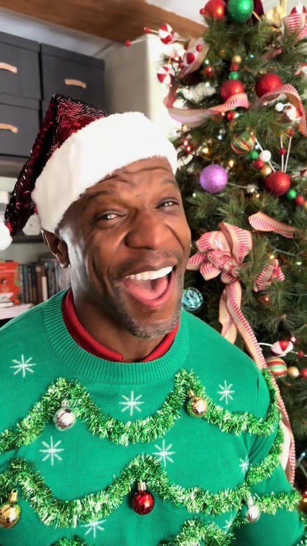 Smiling man in a festive green Christmas sweater and Santa hat by a tree